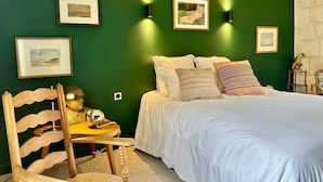 Une chambre avec un mur vert, un lit recouvert d’une literie blanche et plusieurs tableaux encadrés.