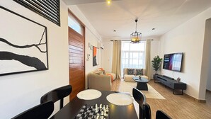 A modern living room with a chessboard on a table, a sofa set, a TV, and a large window with curtains.