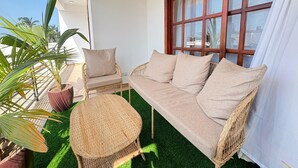 A balcony with a wicker sofa, a wicker chair, and potted plants.