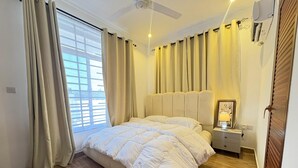 A bedroom with a large bed, a ceiling fan, a bedside table with a lamp, and a window with curtains.