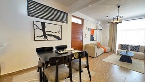 A modern living room with a dining area, featuring a wooden floor, a sofa set, a coffee table, and artwork on the walls.