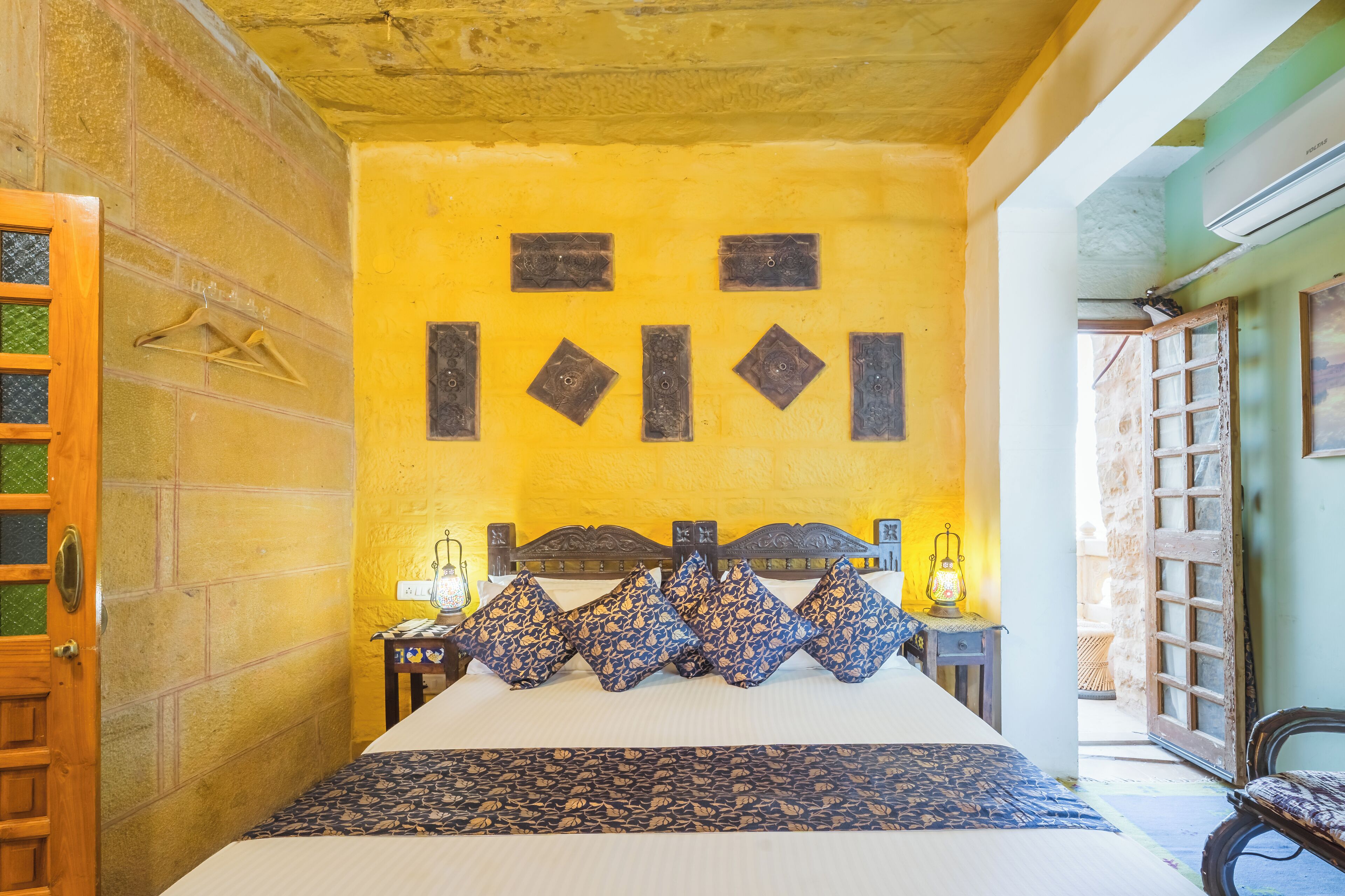 A room with a bed, a wooden door, a wall with geometric patterns, and a hanging light fixture.
