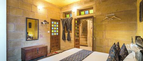 Habitación de hotel con una cama grande, un aparador de madera, un espejo, un ventilador de techo y vistas al exterior a través de la ventana.