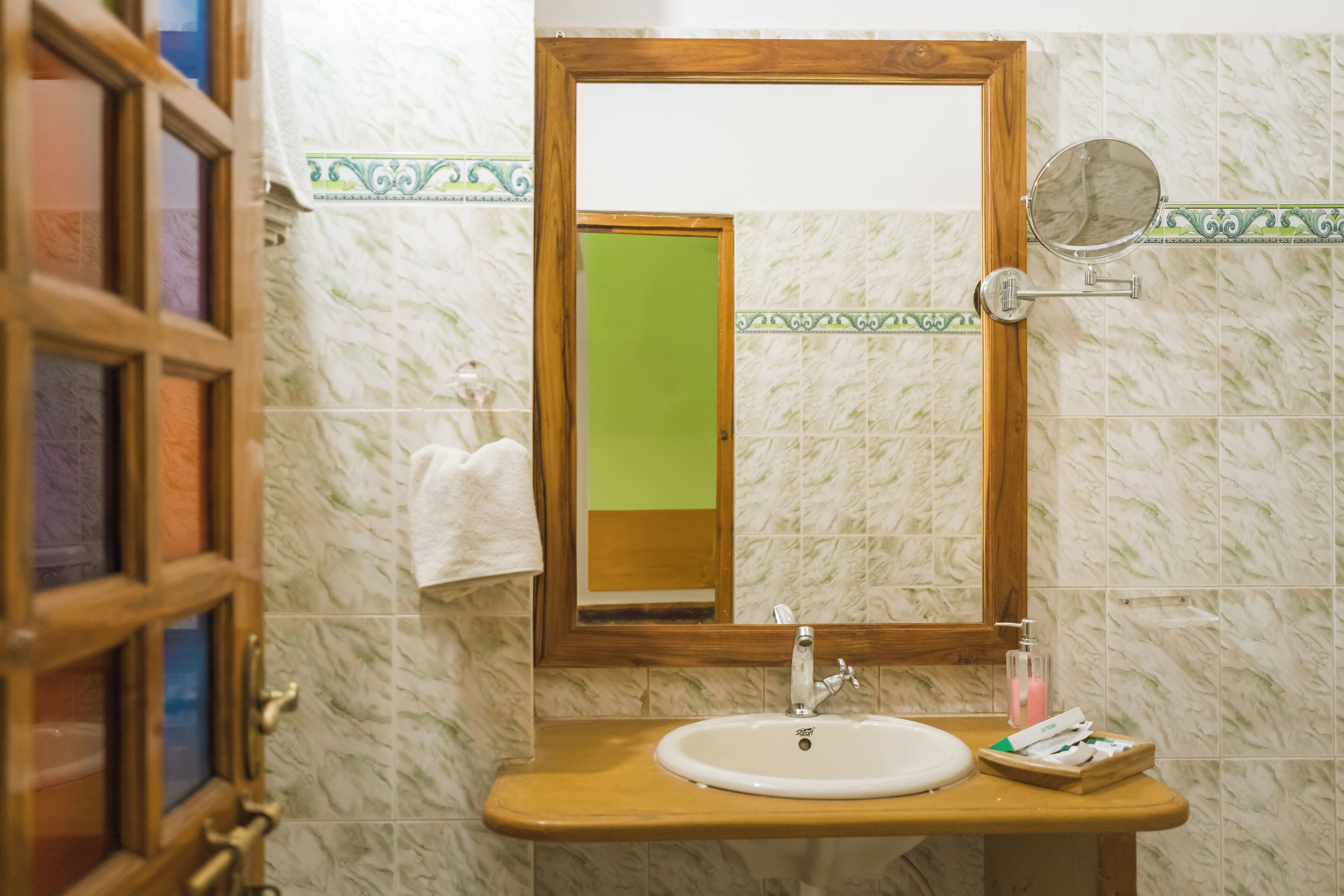 A bathroom with a wooden-framed mirror, a white sink, and a green door.