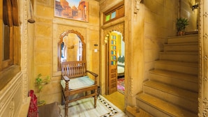 An ornate hallway with a wooden bench, a staircase, and a painting on the wall. - Hotel Rajmandir  (Jaisalmer)