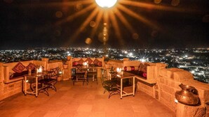 An outdoor dining area with tables and chairs, a large central light fixture, and a city view at night. - Hotel Rajmandir  (Jaisalmer)