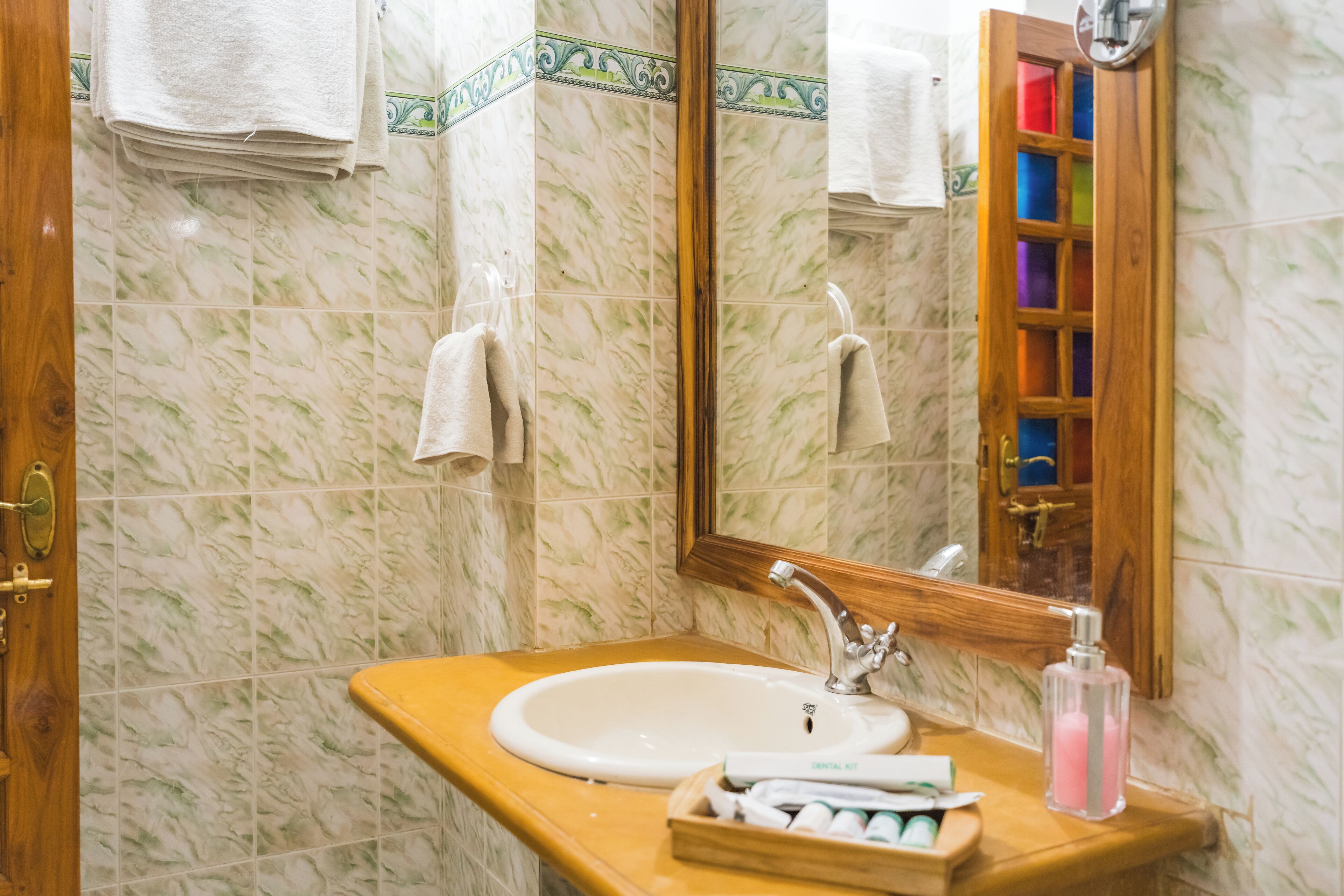 Une salle de bain avec un mur recouvert de carreaux de marbre, un plan-vasque en bois, un miroir et un meuble en bois contenant des articles de toilette.