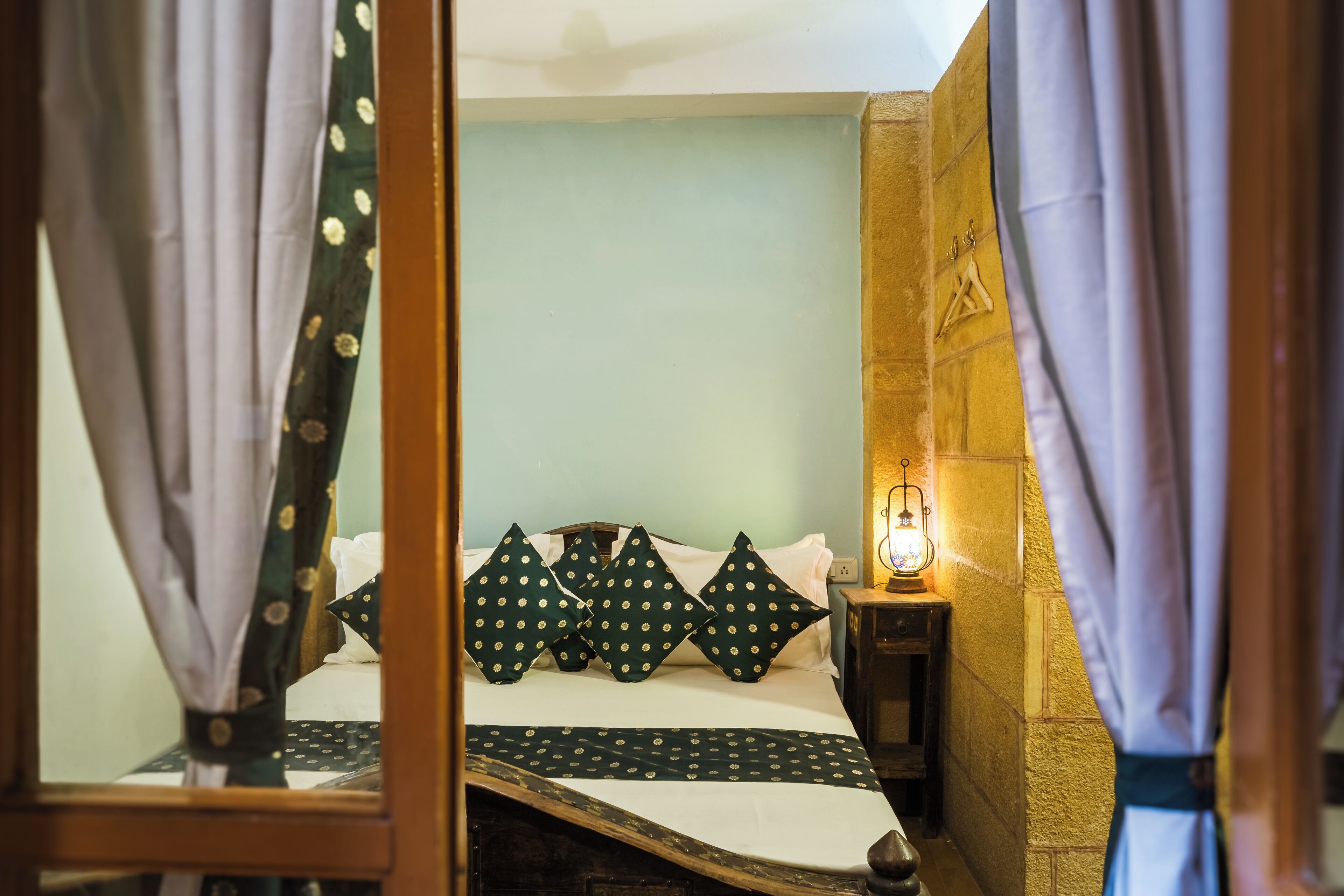A bed with a white and green polka dot bedspread, a wooden headboard, and a small bedside table with a lamp.