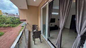 A balcony with a chair and a table, a TV, and a sliding glass door. - RK Homes Service Apartments (Vasco da Gama)
