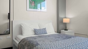 Ein Hotelzimmer mit Bett, Nachttisch mit Lampe, gerahmtem Bild an der Wand und Spiegel.