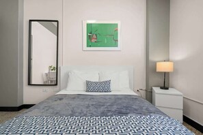 A hotel room with a bed, a nightstand, a lamp, a mirror, and a framed picture on the wall.