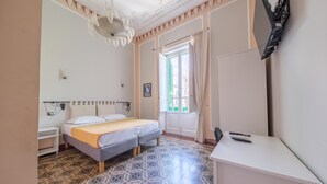 A bedroom with a bed, a desk, a chair, a TV, a window with curtains, and patterned floor tiles. - Epoque Room '1921' with Balcony (Messina)