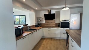 A modern kitchen with white cabinets, a wooden countertop, a built-in oven, and a flat-screen TV.