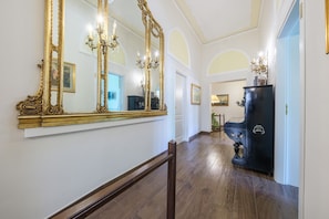 Un couloir orné d’un grand miroir, avec un piano noir et un lustre.