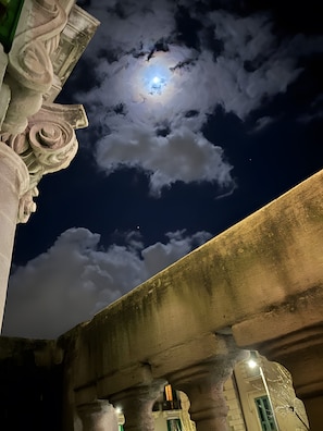 Un ciel nocturne avec une lune visible et des nuages, un pont de pierre et des colonnes d’architecture classique.