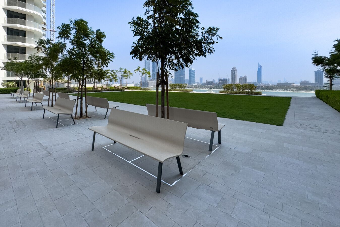 Un espace extérieur aménagé avec des bancs et des arbres, offrant une vue sur un paysage urbain avec des bâtiments modernes.
