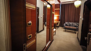 A hotel room with a wooden door, a sofa, a table, and a chandelier.