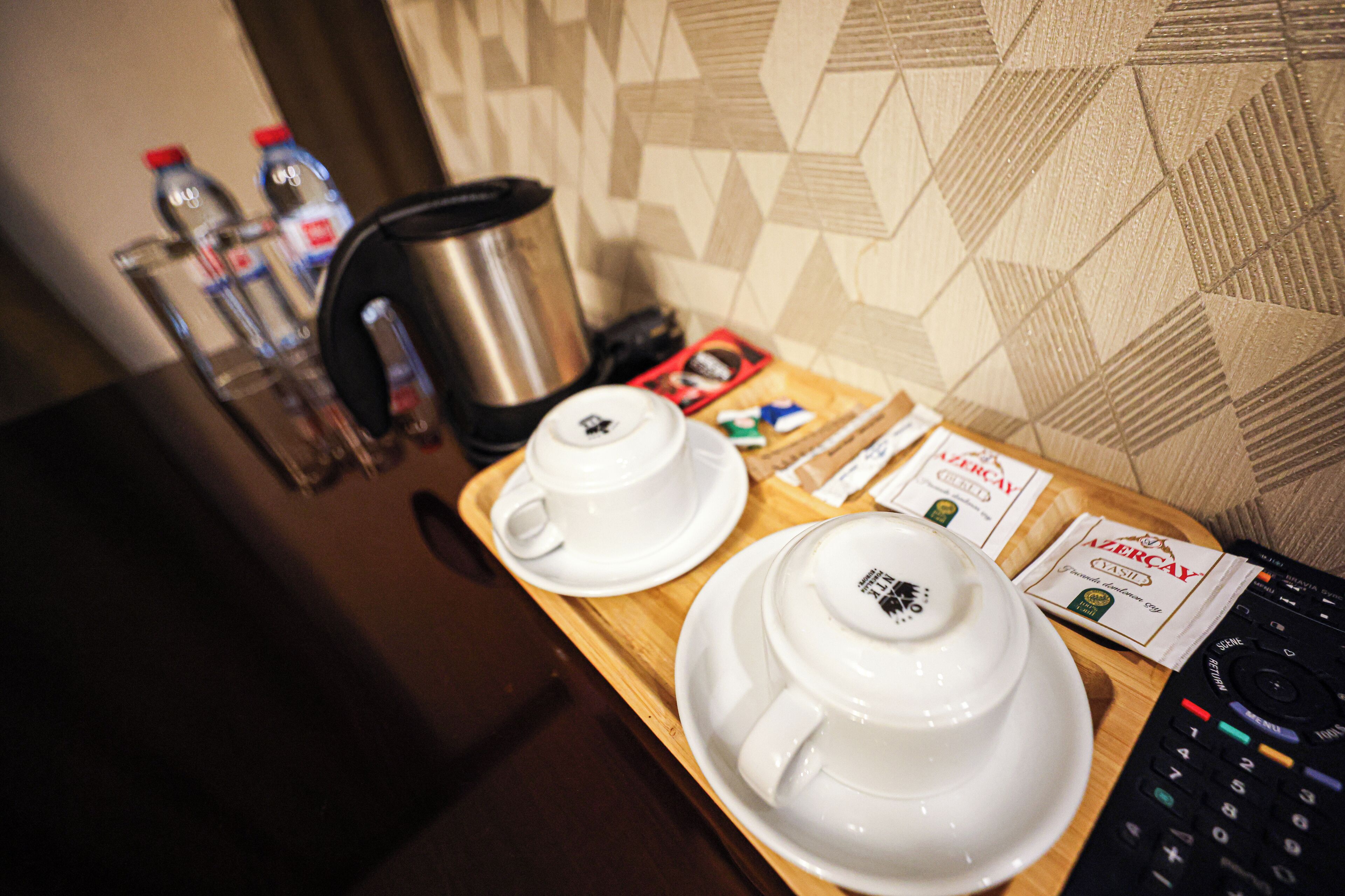 A breakfast tray with two white cups, a coffee pot, and a remote control.