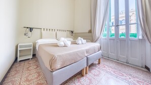 A hotel room with a bed, a nightstand, a wall-mounted lamp, and a window with curtains. - Period Room '1923' with Balcony, Wi-Fi and Air Conditioning (Messina)