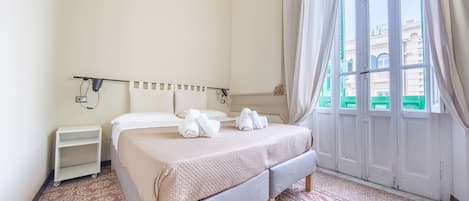 A hotel room with a bed, a nightstand, a wall-mounted lamp, and a window with curtains.