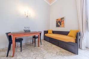 Una habitación con cama, escritorio, dos sillas, una lámpara de pared y un cuadro.