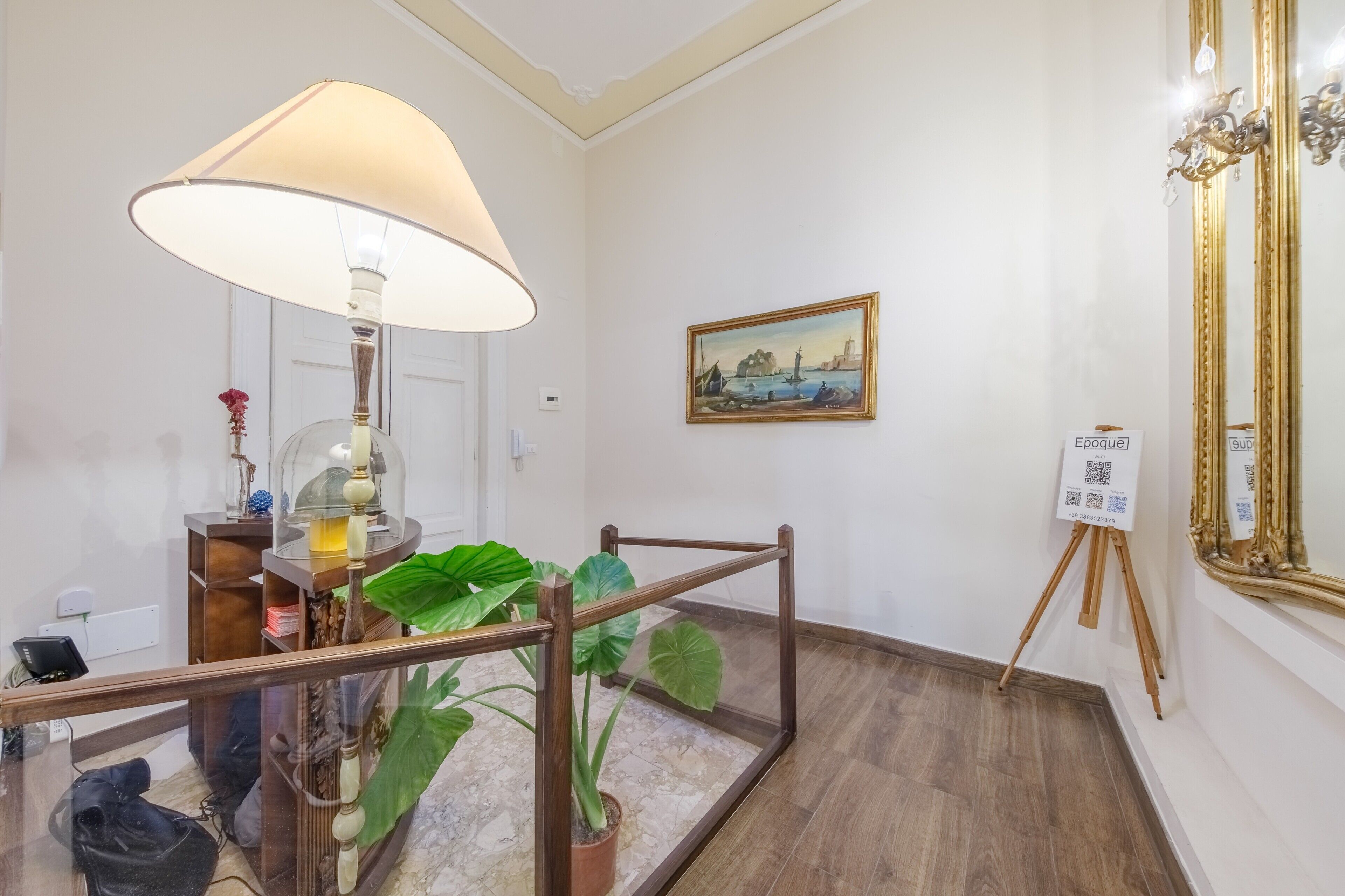 Una stanza con una lampada, un quadro, uno specchio e un cartello con un codice QR.