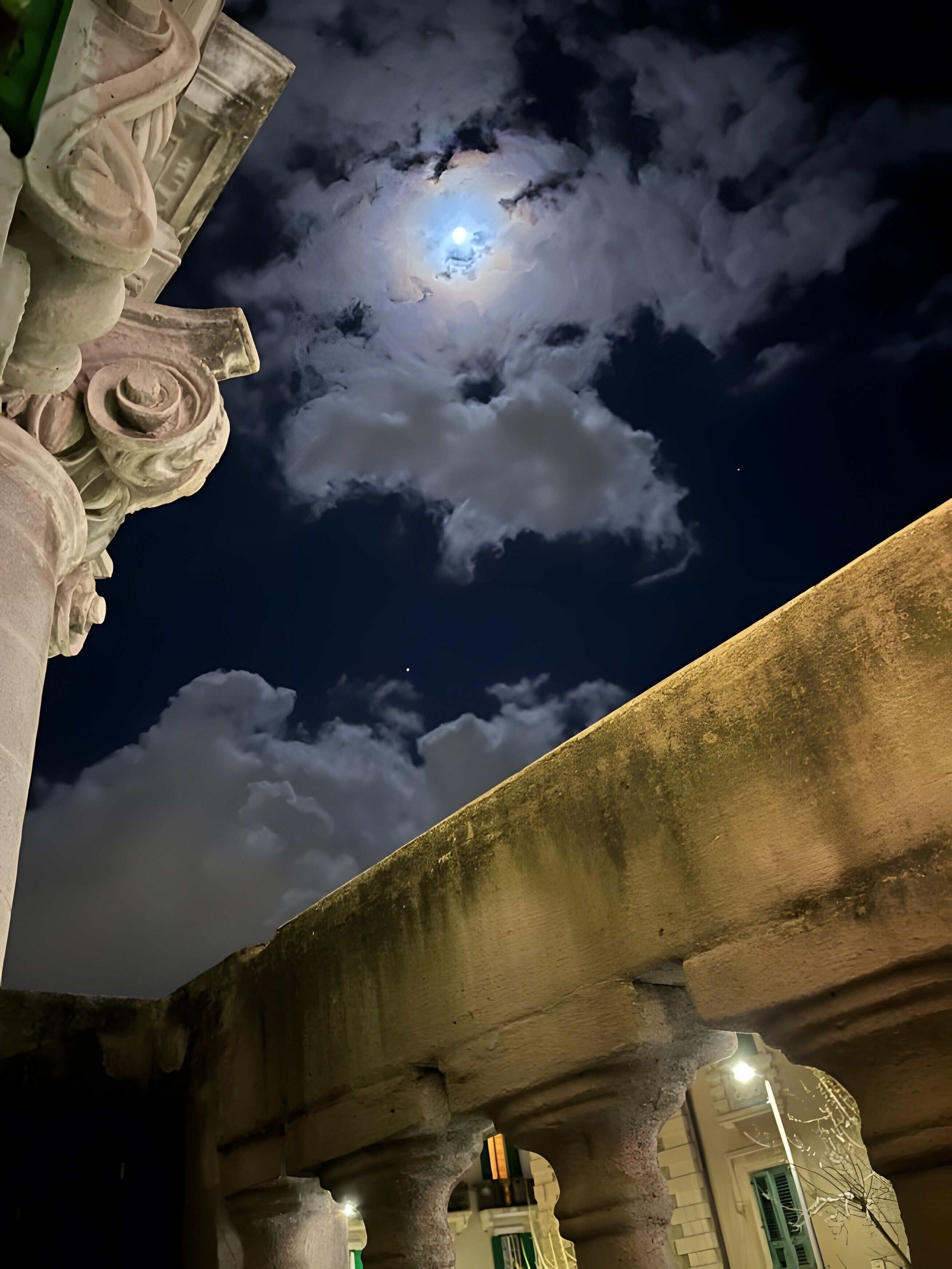 A night sky with a visible moon and clouds, a stone bridge, and classical architectural columns.