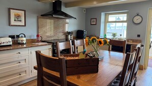 A kitchen with wooden cabinets, a stove, and a dining table with chairs. - Stone &amp; Fleece Cottage (Holmfirth)