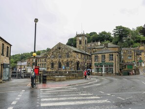 A historic stone building with a clock tower, a red brick road, and a pedestrian crossing. - Stone & Fleece Cottage (Holmfirth)