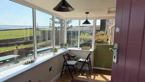 A room with large windows, a view of a green field, a wicker basket, and a door with a handle. - Stone &amp; Fleece Cottage (Holmfirth)