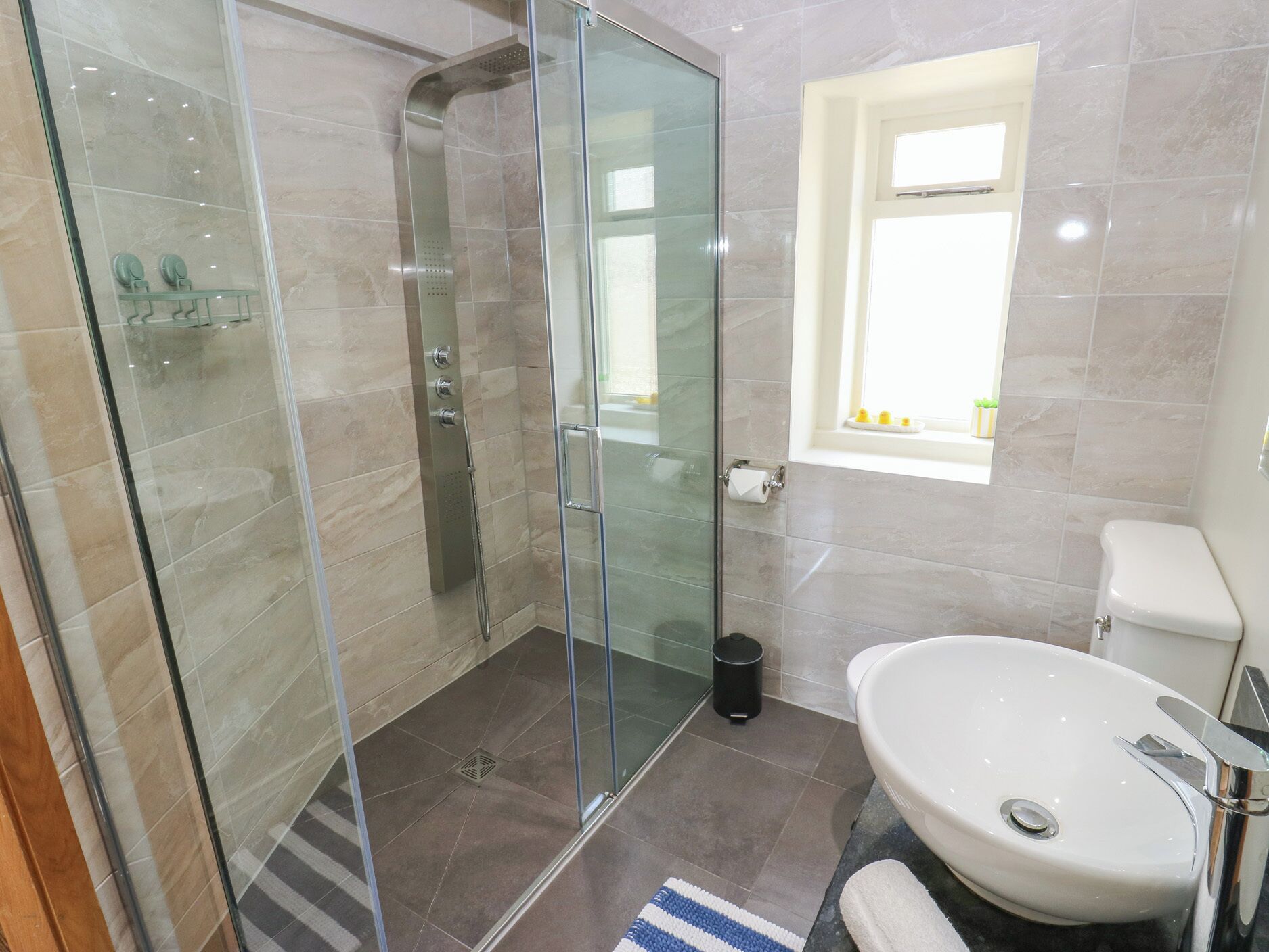 A modern bathroom with a glass-enclosed shower, a white sink, and a small window.