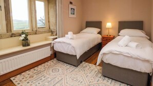 A bedroom with two beds, a window with a view, a radiator, and a patterned rug. - Stone &amp; Fleece Cottage (Holmfirth)