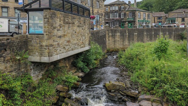 A stone bridge over a flowing river, with buildings on either side, including a clock tower. - Stone &amp; Fleece Cottage (Holmfirth)