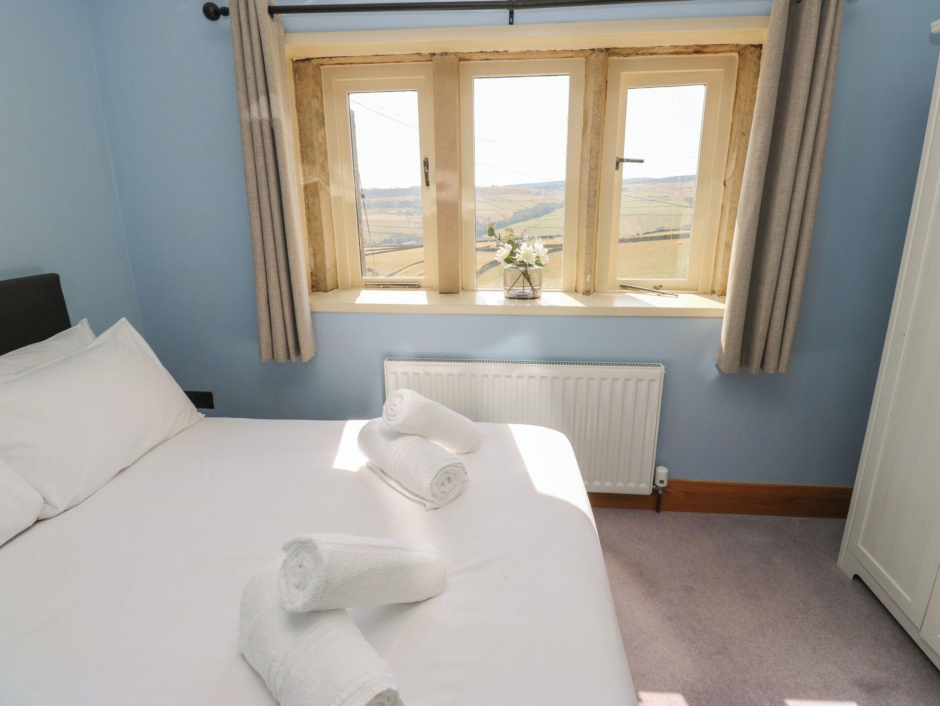 A hotel room with a large bed, a window with curtains, a radiator, and a view of the countryside.