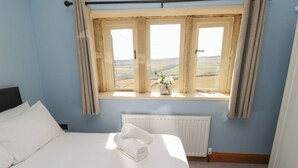 A hotel room with a large bed, a window with curtains, a radiator, and a view of the countryside. - Stone & Fleece Cottage (Holmfirth)