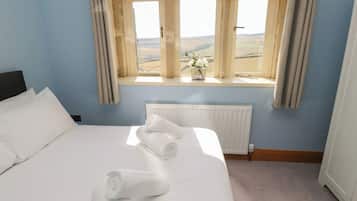 A hotel room with a large bed, a window with curtains, a radiator, and a view of the countryside.