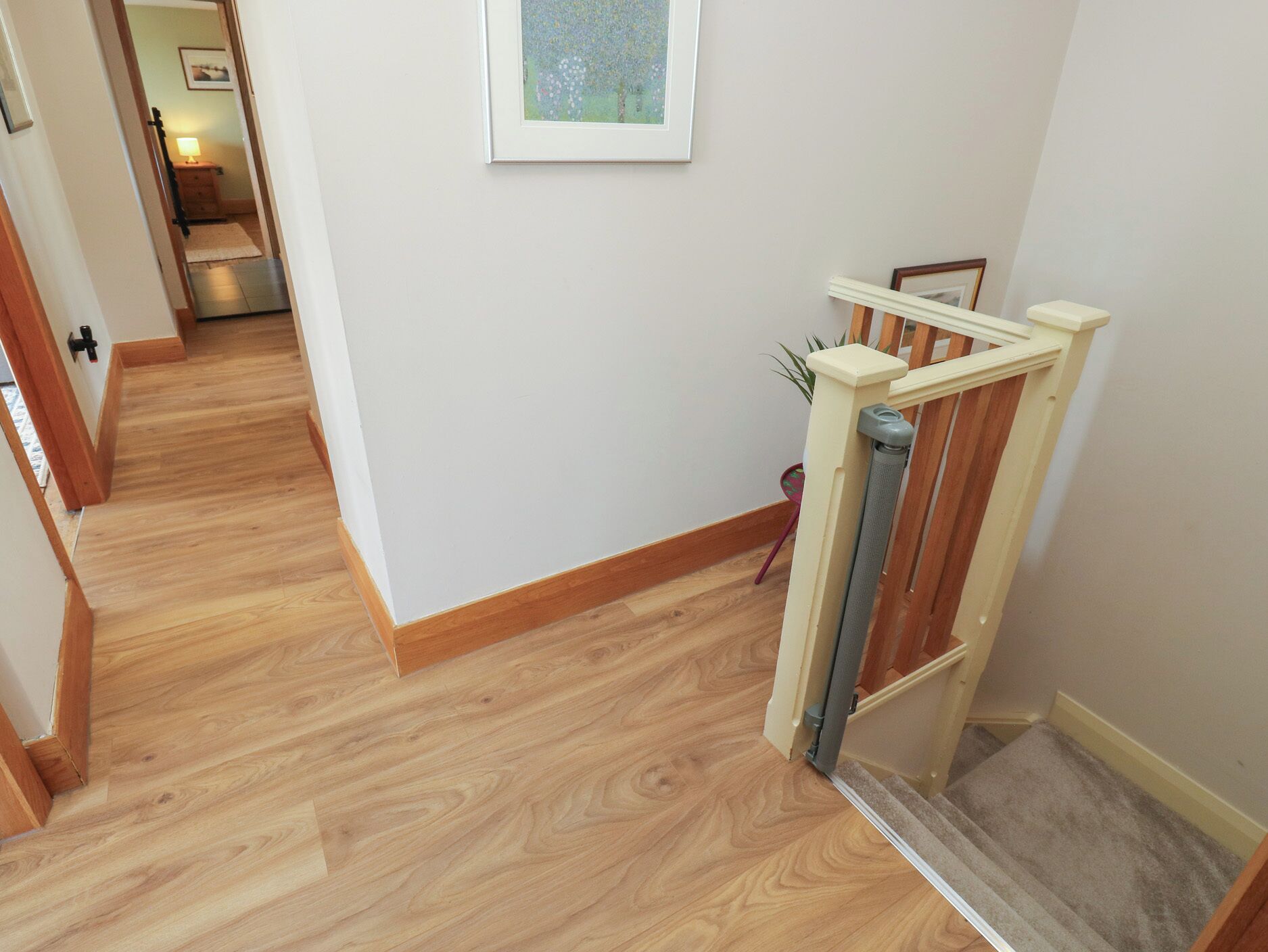 A hallway with wooden flooring, a staircase with a handrail, and a framed picture on the wall.