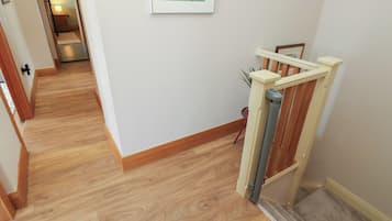 A hallway with wooden flooring, a staircase with a handrail, and a framed picture on the wall.