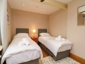 A hotel room with two single beds, a nightstand with a lamp, and a mirror on the wall. - Stone &amp; Fleece Cottage (Holmfirth)