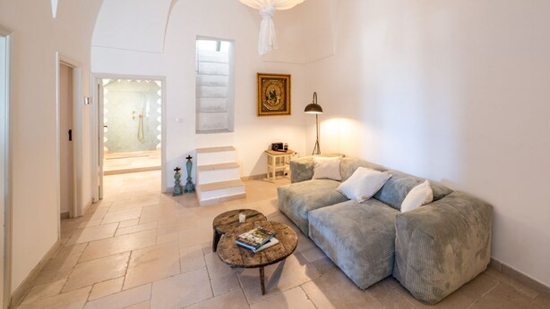 A spacious living room with a large sofa, a coffee table, and a staircase leading to a balcony.