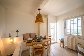 A dining area with a table set for two, a hanging light fixture, a window with a view, and a radiator.