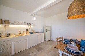 A kitchen with white cabinets, a refrigerator, a dining table with blue and white plates, and a hanging light fixture.