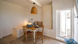 A dining area with a table set for two, a hanging light fixture, and a view through a door.
