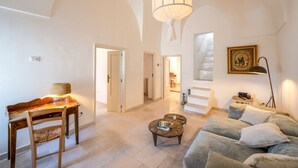 A spacious living area with a wooden desk, a sofa, a coffee table, and a staircase leading to an upper level.