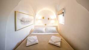 A cozy, arched room with a bed, two towels, a framed feather artwork, and wall-mounted lights.