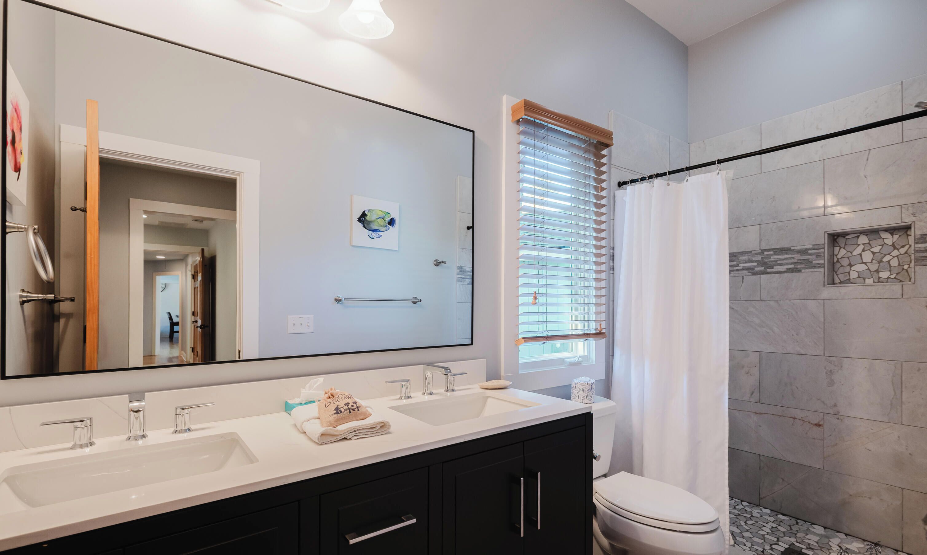 Une salle de bain avec un grand miroir, deux lavabos, des toilettes et un rideau de douche.