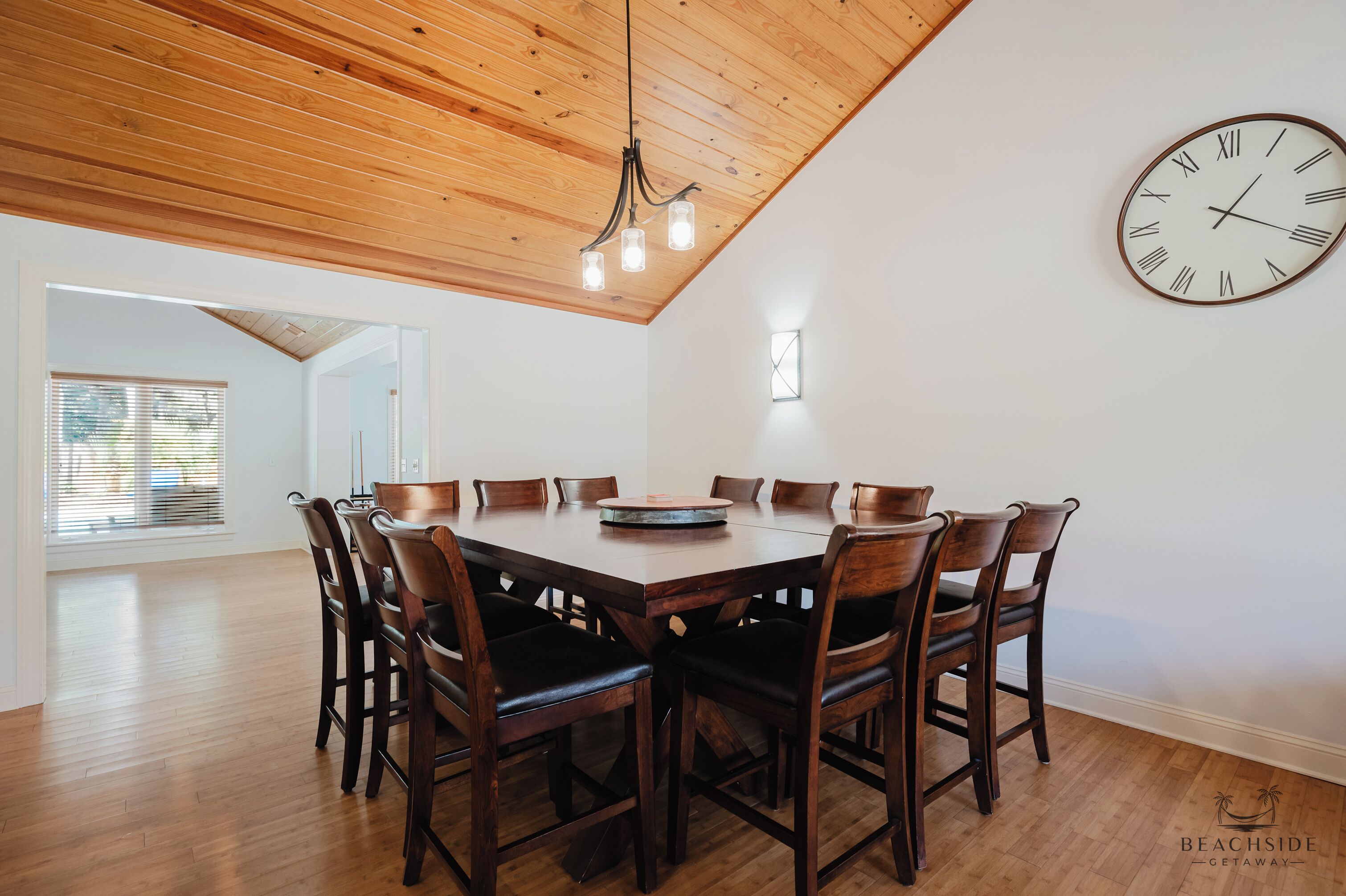A dining area with a wooden ceiling, a round table, and eight chairs.
