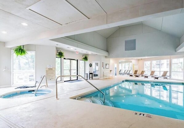 Une piscine intérieure dont la profondeur maximale est de 3 pieds, avec des chaises longues et des plantes en pot.