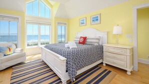 Ein Schlafzimmer mit einem großen Bett, einem Nachttisch, einer Kommode und einem Fenster mit Blick auf das Meer.
