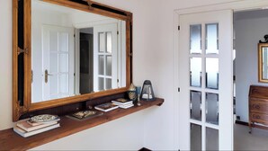 Une pièce avec un grand miroir, une étagère en bois remplie de livres, une lanterne et une commode.